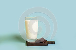 A glass of milk and pieces of dark chocolate on a wooden stand