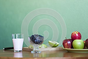 A glass of milk, a plate of apples, a bowl of blueberries on a green background