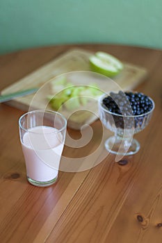 A glass of milk, a plate of apples, a bowl of blueberries on a green background