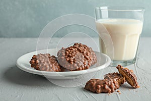 Glass of milk and plate with chocolate cookies on grey table