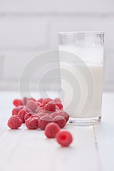 Glass of milk and ripe raspberries. White background