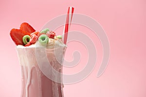 Glass of milkshake with ice cream, colorful candies, strawberry halves and drinking tube