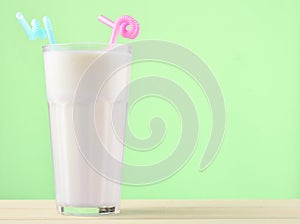 A glass of milkshake with a straw on a pastel color wooden table.