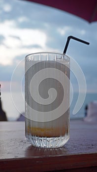 A glass of milkshake on a table with straws on a beach background