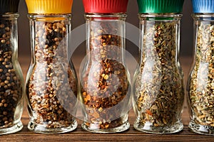 Glass mills with aromatic spices and herbs. Several grinders of different seasoning closeup. Condiments for cooking