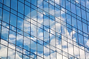 Glass mirror skyscraper wall with blue sky and white clouds reflection close up, modern business center view