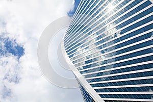 Glass mirror skyscraper wall spiral shape on blue sky, white clouds background, modern business center building