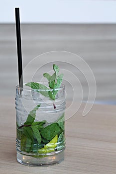 Glass of mochito cocktail on wooden table with black straw, ice and mint leaf