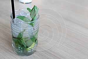 Glass of mochito cocktail on wooden table with black straw, ice and mint leaf