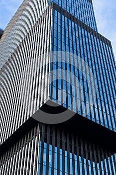 Glass modern skyscraper with blue sky background. Low angle view and architecture details. Windows of glass office building.