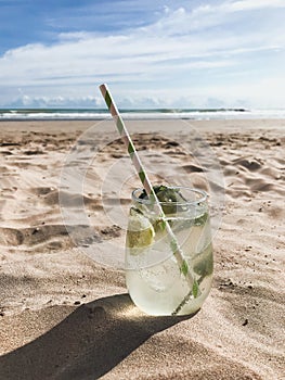 A glass with a mojito cocktail stands on an empty sandy beach against the sea