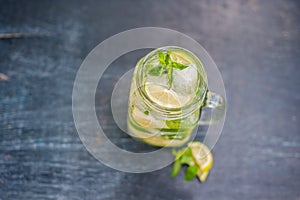 Glass of mojito with lime and mint ice cube close-up on dark wood background