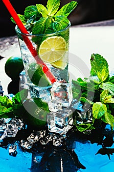 Glass of mojito with lime and mint ice cube close-up red straw on blue background