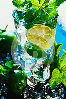 Glass of mojito with lime and mint ice cube close-up red straw on blue background