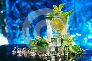 Glass of mojito with lime and mint ice cube close-up red straw on blue background