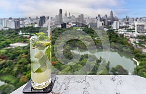 glass of mojito on the roof top bar table with Bangkok city vier and park