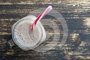 Glass mug of chocolate milkshake on wooden background. Top view, copy space