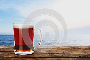 Glass mug of delicious kvass on wooden table near sea. Space for text