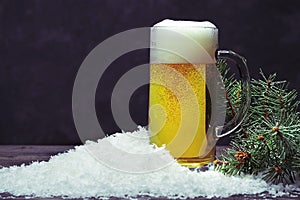 Glass mug of beer in the snow on a dark background.