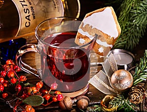 Glass mug of grog lying next to red wine bottle .