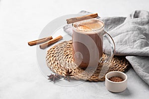 Glass mug with hot chocolate and milk foam on a light background with cinnamon sticks, anise star and cocoa powder