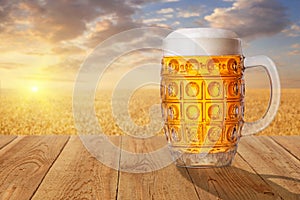 Glass mug of beer against wheat field