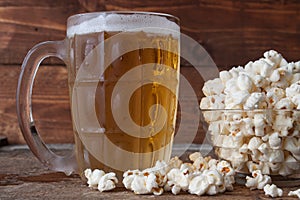 Glass mug of light beer with popcorn on wooden table, close up