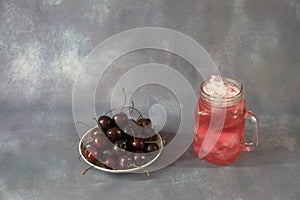 Glass mug of red juice and trill full of ripe cherries on a gray background