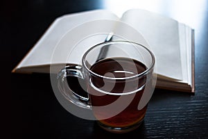 A glass mug with tea and a lemon slice, notebook with blank pages, black pen on dark desk