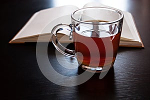 A glass mug with tea and a lemon slice, notebook with blank pages, black pen on dark desk