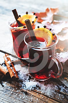 Glass mugs of mulled wine on table with autumn leaves and snow.