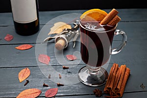 Glass of mulled wine, bottle of wine and corkscrew with open cork on wooden table.