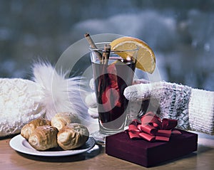 Glass of mulled wine, Christmas balls, white hat and woman gloved hand, croissants and gift box