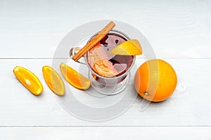 Glass with mulled wine or hot cider near juicy orange fruit on white background. Drink or beverage with orange and