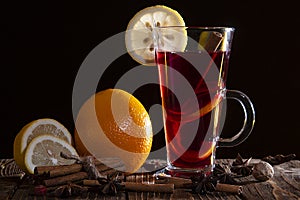 A glass of mulled wine with an orange peel and a slice of lemon, cinnamon sticks, star anise and sliced citrus fruits on a wooden