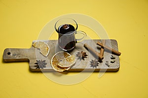 A glass of mulled wine on a wooden board with cinnamon sticks and lemon. Top view. Yellow background