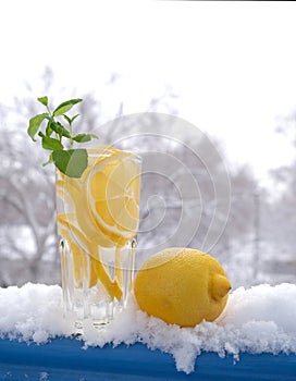 Glass with natural lemon drink with a sprig of mint in the snow