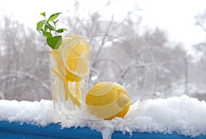 Glass with natural lemon drink with a sprig of mint in the snow