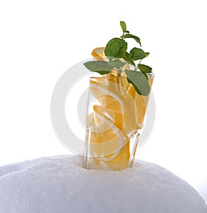 Glass with natural lemon drink with a sprig of mint in the snow