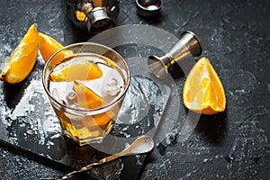 A glass of Negroni cocktail with orange and lemon. Alcoholic drink with rum and vermouth on dark stone table