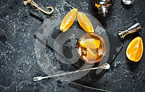 A glass of Negroni cocktail with orange and lemon. Alcoholic drink with rum and vermouth on dark stone table.