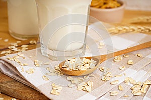 A glass of oat milk a jug and oat flakes on a wooden background