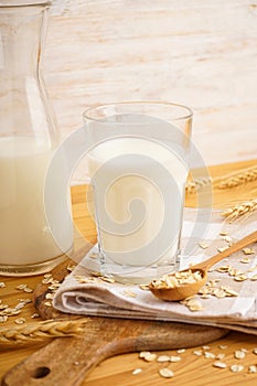 A glass of oat milk a jug and oat flakes on a wooden background. Vertically