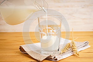 A glass of oat milk, a jug and towel on wooden background