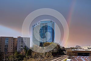 Glass office buildings and apartments along a side a set of railroad tracks with blue sky and powerful clouds and a rainbow