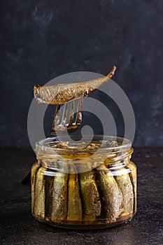 Glass open jar of sprots and fish on a fork