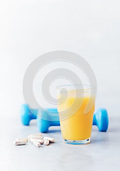 Glass of Orange Juice. Blue Dumbbells and Sport supplements  Carnitine capsules  in background.