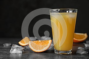 Glass of orange juice with ice cubes and cut fruit on table against black background