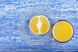 A glass of orange juice near which lay sliced oranges. View from above
