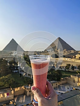 A glass of orange juice overlooking the Great Pyramid of Giza and the Pyramid of Khafre